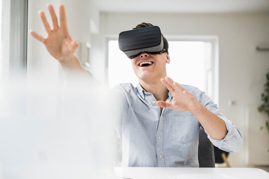 Cheerful male professional wearing wearing virtual reality simulator while sitting at desk in home office