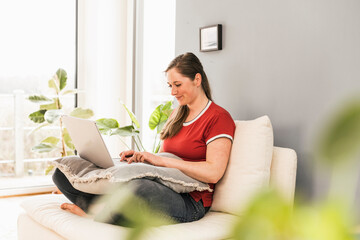 Woman sitting on sofa using laptop at home