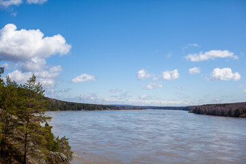 Beautiful, wide autumn river among forests and rocky shore. A calm and quiet place with autumn colors. Reflection of clouds in the water in good weather