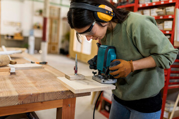 Female carpenter working with router jig at workbench in industry