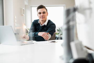 Smiling young businessman sitting at desk in home office