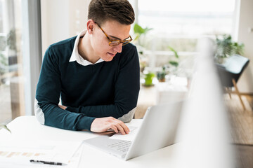 Businessman wearing eyeglasses reading document while sitting at desk