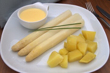 white plate with three white asparagus, potatoes and sauce hollondaise