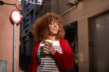 Beautiful woman with disposable coffee cup smiling while standing against street