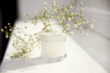 mockup moisturizer cream in glass jar and gypsophila on white background. Natural organic spa cosmetics concept.