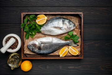 Raw dorado fish with lemon and parsley in a dish on the table. Top View