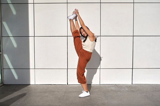 Young woman practicing standing splits against wall
