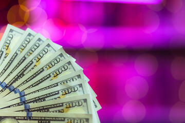One hundred dollar bills on a pink background with a beautiful bokeh. The theme of cash settlement in a brothel or casino. USD money in macro photography in purple lighting. With a copy space place.
