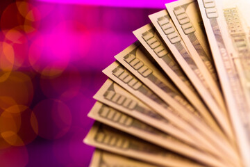 Many hundred dollar bills on a pink background with a beautiful bokeh. The theme of cash settlement in a brothel or casino. USD money in macro photography in purple lighting.
