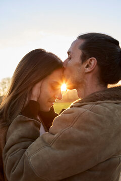 Man kissing on girlfriend's forehead against sky during sunset