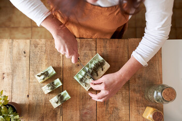 Woman cutting pieces of organic handmade soap on cutting board at workshop