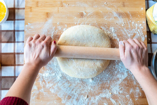 Woman rolling dough on cutting board for making croissants in kitchen