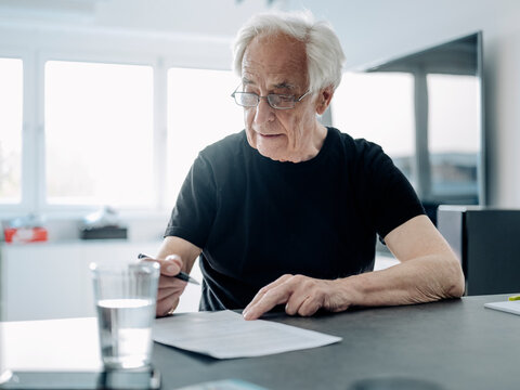 Businessman wearing eyeglasses writing in paper while sitting at office