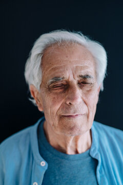 Senior man standing with eyes closed against black background