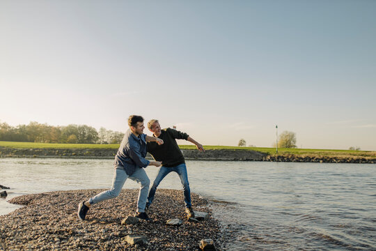 Father and son throwing pebbles in river against clear sky during autumn