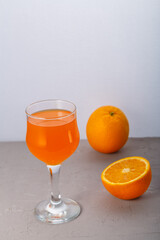 Orange juice in a glass near oranges on a gray background.