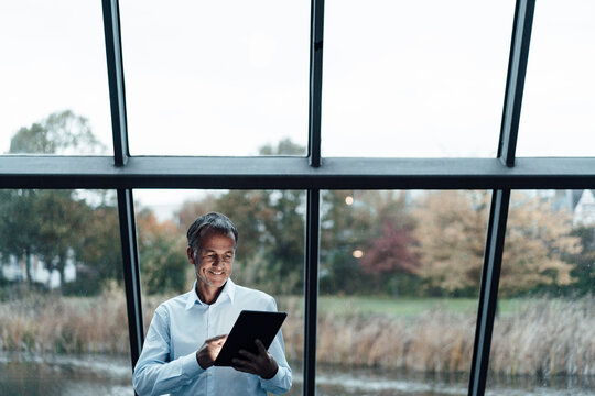 Smiling senior business professional using digital tablet against glass window
