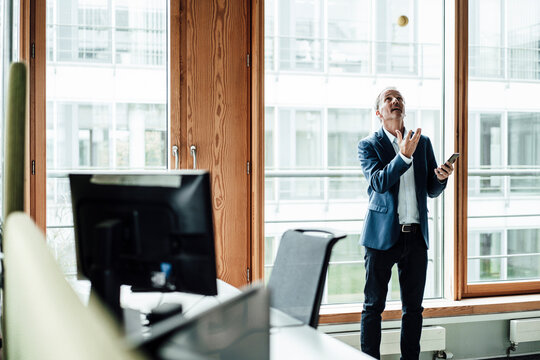 Playful businessman throwing ball against glass window in office