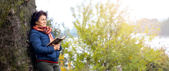 Elderly woman with a book in her hands on the nature. Reading in nature. Rest in the woods. Reading the Bible. Unity with nature