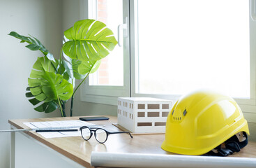 Hardhat with architectural model and eyeglasses on desk against window