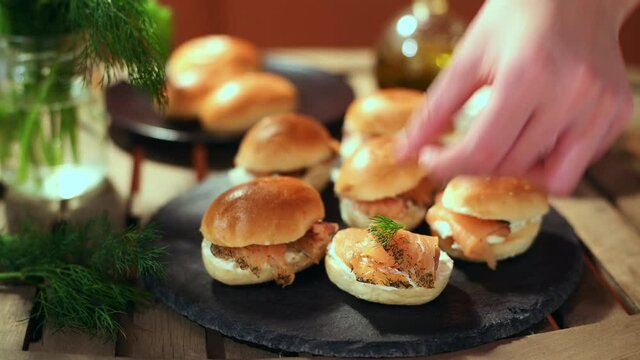 Preparation of Plate of salmon canapes marinated with cheese on table with woman's hand adding dill branch on sandwich of salmon marinated with cheese
