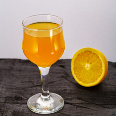 Orange juice in a glass near oranges on a black background.