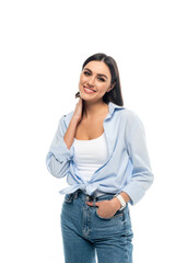 happy woman in blue shirt touching neck while posing with hand in pocket isolated on white.