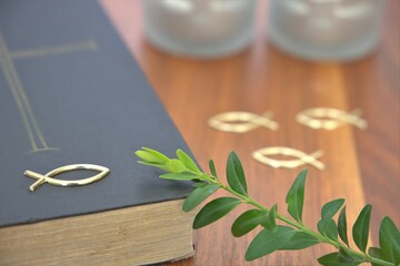 decoration for church confirmation with bible and fish symbol and a branch of bux on a table , focus on foreground