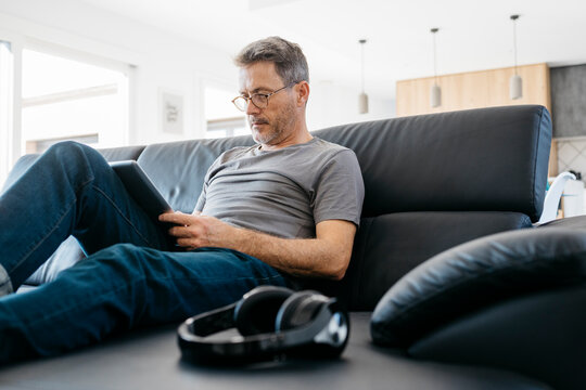 Mature man using digital tablet while sitting on sofa in living room