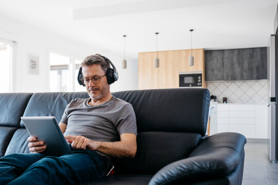 Mature man with headphones using digital tablet while sitting on sofa at home