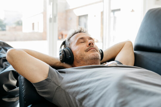 Mature man listening music through headphones while relaxing on sofa in living room