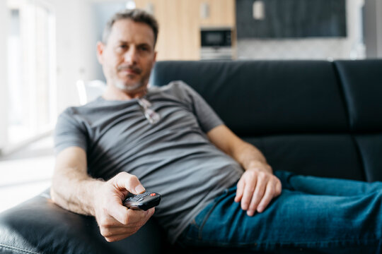 Mature man changing channels through remote control on sofa in living room