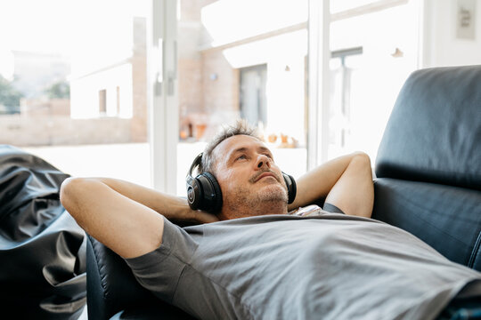 Mature man listening music through headphones while lying on sofa in living room