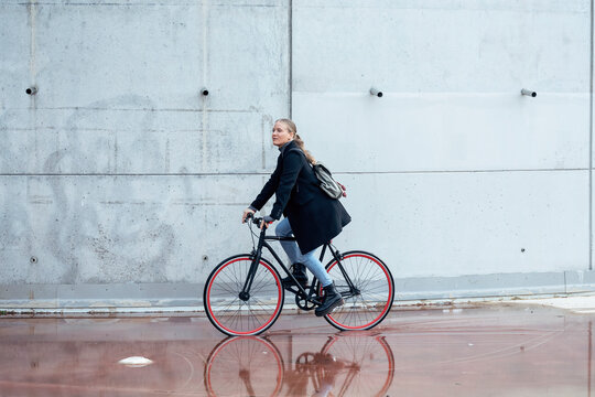 Woman doing cycling on wet road by wall