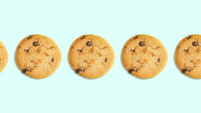 Stop motion animation. Lots of American round cookies with chocolate pieces moving along a line on a blue background
