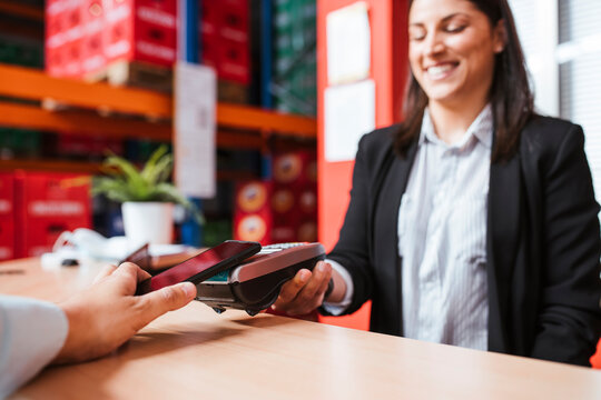 Smiling female manager holding card reader for customer with smart phone