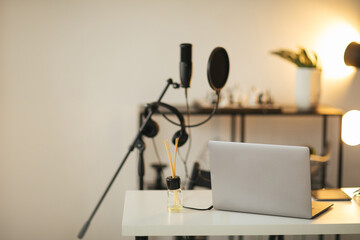 Items for recording podcast: professional microphone, earphones and laptop on white table in studio with white walls.