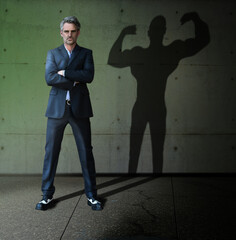 Obraz premium Super leader business man in a suit with strong man shadow - self-assessment. Muscular career leader.