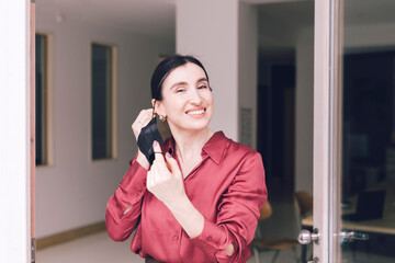 Smiling businesswoman removing protective face mask while standing at glass door during pandemic