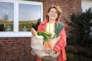 Beautiful redhead woman holding bag of groceries against wall