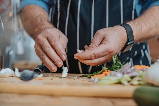 Male chef wearing apron peeling garlic while doing preparation standing in kitchen
