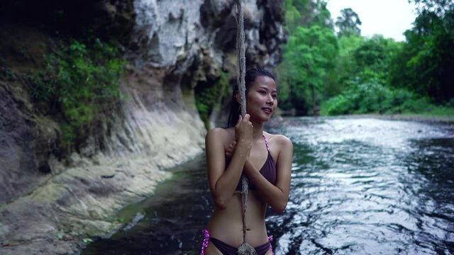 Cute Smiling Asian Girl in Bikini in the River by a rope, Thailand.