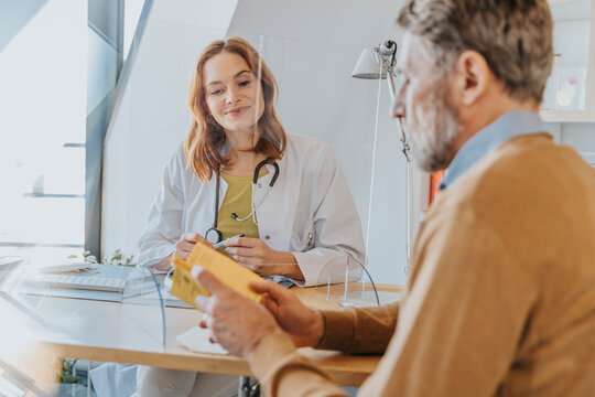 Male patient discussing over vaccination certificate with doctor while sitting at office during COVID-19