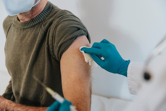 Healthcare worker cleaning arm of male patient while preparing for vaccination at examination room