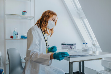 Doctor wearing protective face mask checking medical test while sitting at examination room
