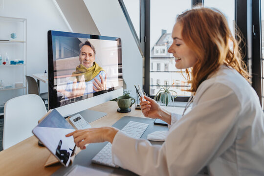 Smiling patient talking to doctor through computer while sitting at office