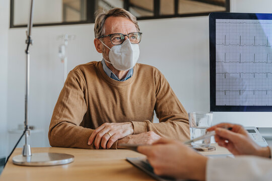 Male patient wearing protective face mask looking at doctor while sitting at clinic