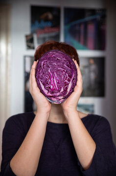 Woman holding a red cabbage in front of her face