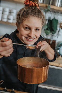 Smiling chef tasting broth soup in saucepan while standing in kitchen