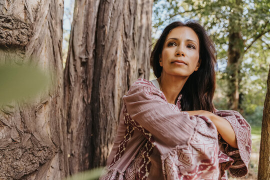 Woman looking away while sitting under Robinia Pseudoacacia tree at park